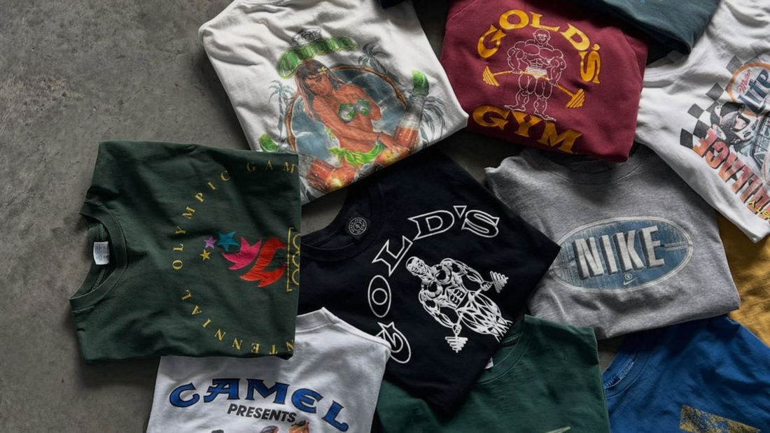 T-shirt vintage piegate di Gold's Gym, Nike e altri marchi, impilate su cemento.