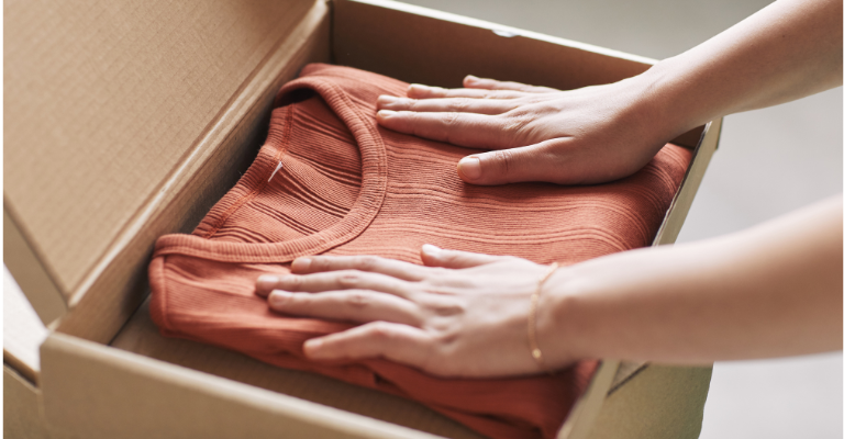 Mani di un venditore che piegano con cura una maglia all'interno di una scatola di cartone per la spedizione.